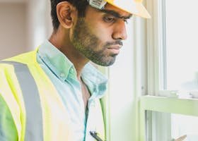 Professional construction worker examines property indoors with clipboard, ensuring safety compliance.